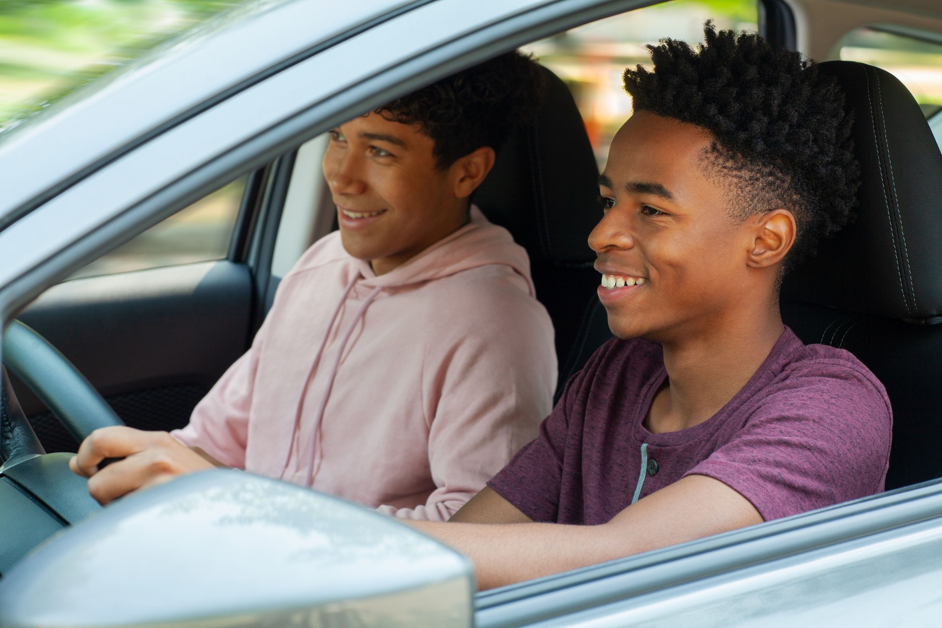 Young Black ethnicity teenager boy driving car while Multiracial Hispanic Caucasian friend sits in car with friend passenger