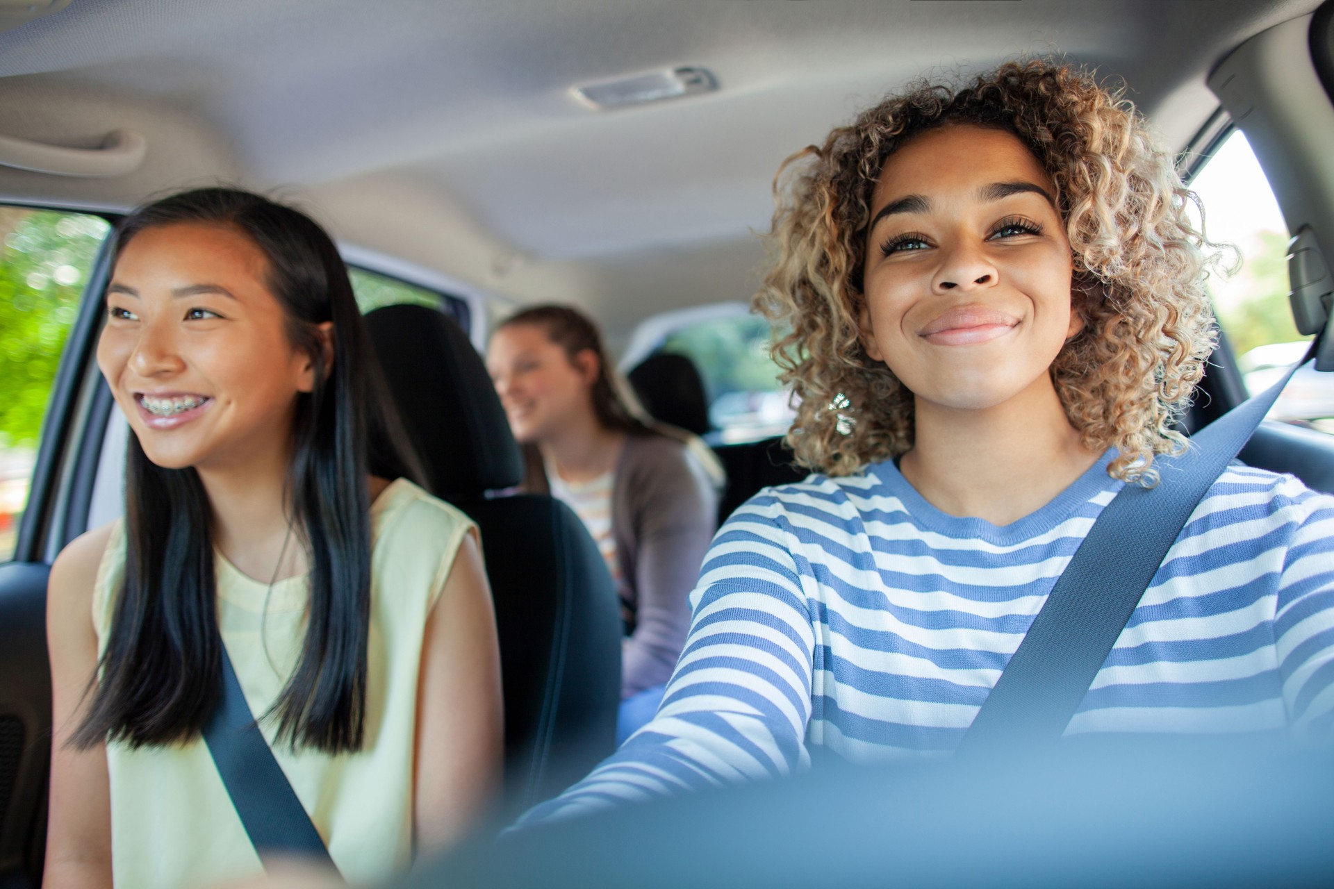 Young Multiracial teenager girl driving car while Asian Chinese friend sits in car with friends passenger